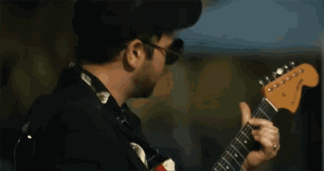 a man wearing sunglasses and a hat plays a guitar