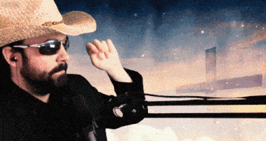 a man wearing a cowboy hat and sunglasses stands in front of a microphone