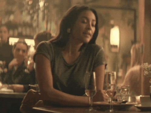 a woman sits at a table with two wine glasses