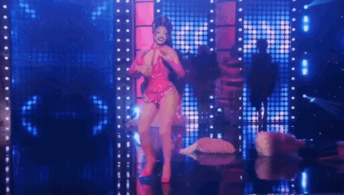 a drag queen is dancing on a stage in front of a blue and pink background .
