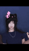 a girl wearing a hello kitty hat and a necklace is standing in front of a blue wall .
