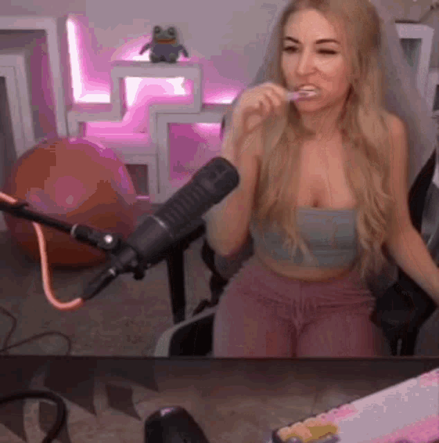 a woman is brushing her teeth in front of a microphone while sitting in front of a desk .