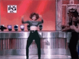 a woman in a crop top is dancing in front of a tv pg dl sign