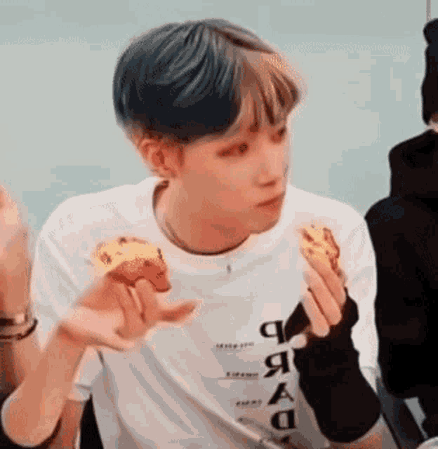 a young man with blue hair is eating a piece of pizza while sitting at a table .