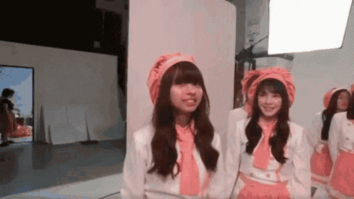 a group of girls are standing next to each other in a room wearing pink clothes and hats .
