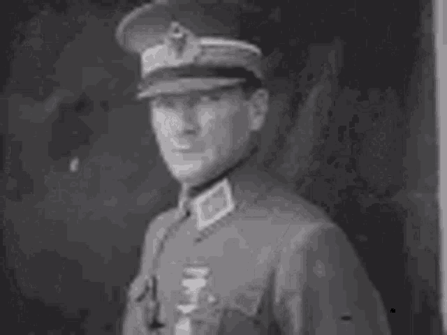 a man in a military uniform and hat is standing in front of a painting .