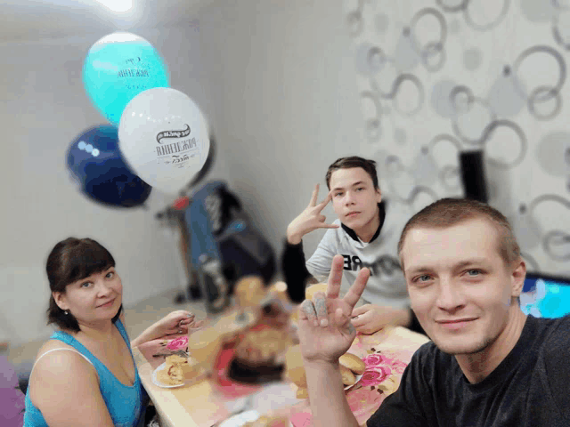a group of people sitting at a table with balloons in the background one of the balloons says " khleb and "