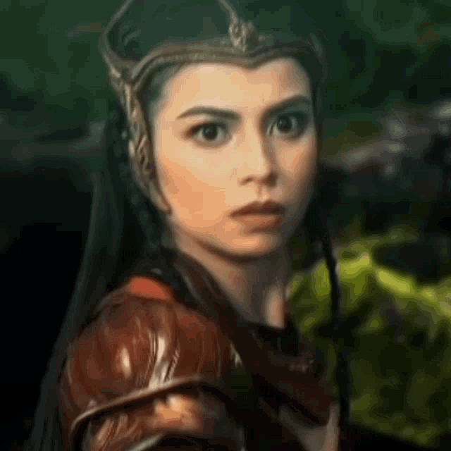 a close up of a woman wearing a crown and armor looking at the camera .