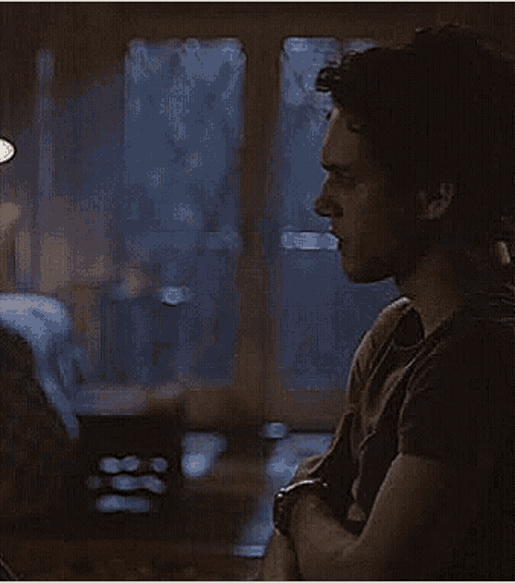 a man is sitting in front of a window in a dark room looking out the window .