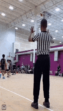 a referee in a black and white striped shirt stands in front of a purple wall that says upc