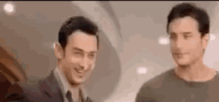 two men are standing next to each other in a room and smiling at each other .