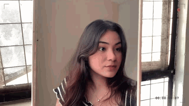 a girl is standing in front of a window with the time of 00 : 00 : 30 : 07 on the bottom right
