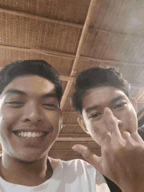 two young men are posing for a picture and one is smiling and the other is giving the middle finger