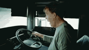 a man in a green shirt is driving a truck with his mouth open
