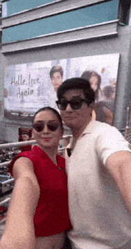 a man and woman taking a selfie in front of a hello love again billboard