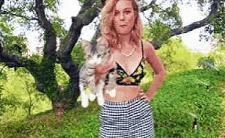 a woman in a bikini top and plaid skirt is holding a kitten .