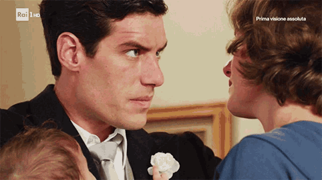 a man in a suit holds a baby while a woman looks on and the words prima visione assoluta are visible