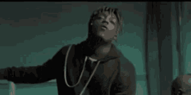 a man in a black hoodie is standing in a dark room with his arms outstretched .