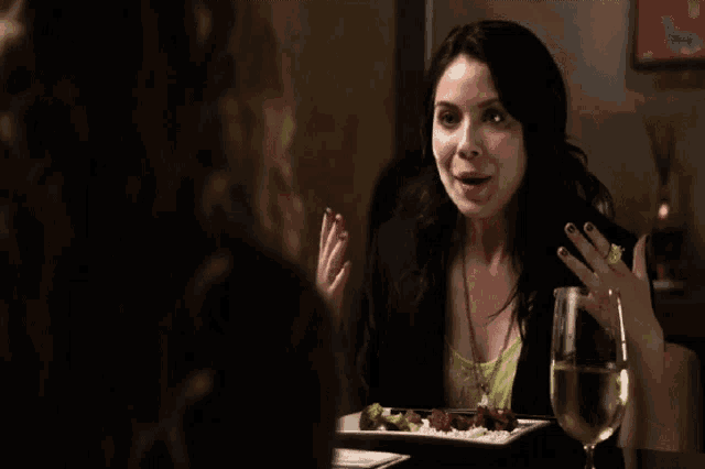 a woman sitting at a table with a plate of food and a glass of white wine