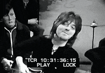 a black and white photo of a man playing a guitar in a room with other people .