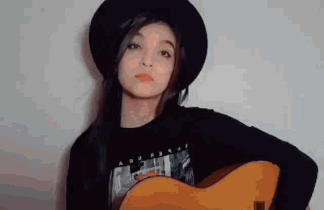 a young girl is holding a guitar and wearing a black hat .