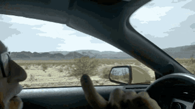 a person is driving a car in the desert and giving a thumbs up