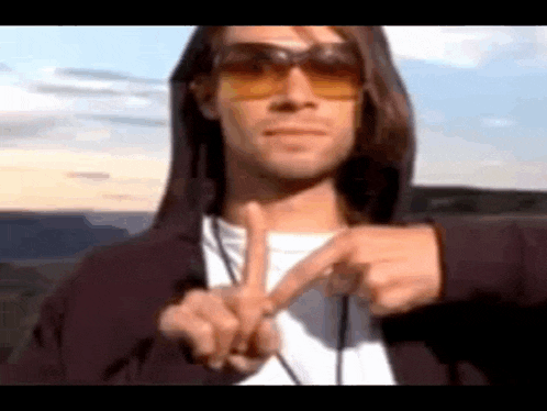 a man wearing sunglasses and a hoodie is making a peace sign with his hands .