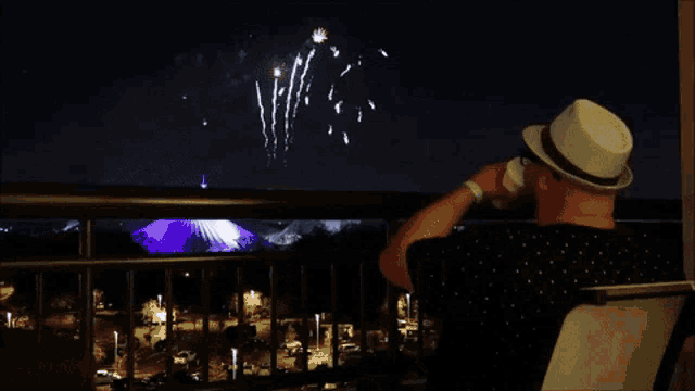 a man sitting on a balcony watching fireworks over a city
