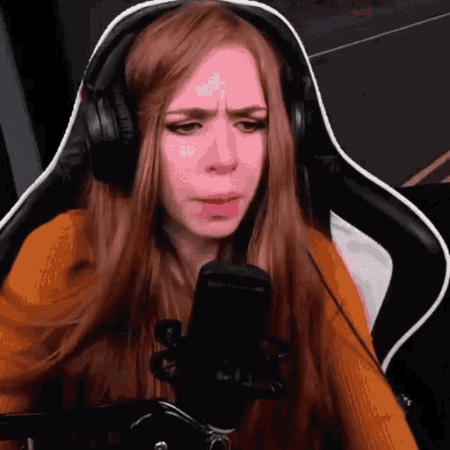 a woman wearing headphones is sitting in front of a microphone and making a face