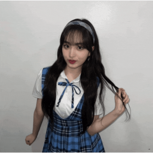 a girl wearing a blue and white plaid dress holds her hair