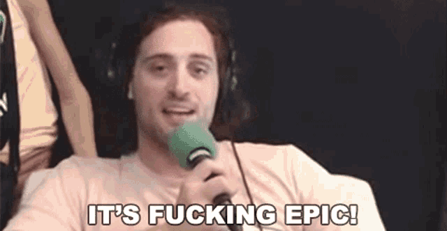 a man wearing headphones is holding a green microphone and saying it 's fucking epic .