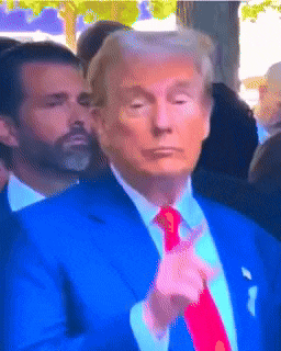 donald trump in a blue suit and red tie giving a peace sign