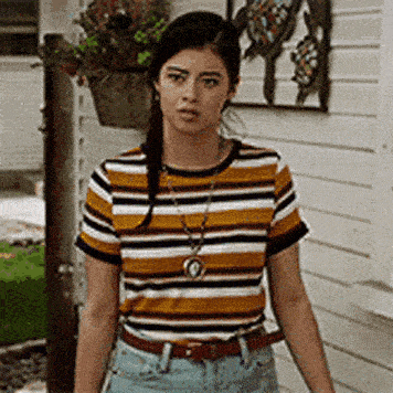 a woman wearing a striped shirt and jeans is standing in front of a white building .