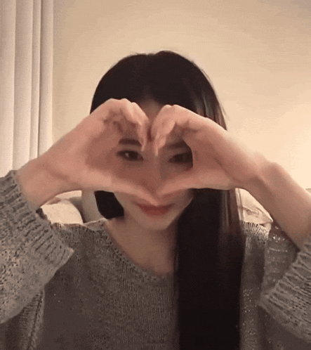 a woman making a heart shape with her hands in front of her face