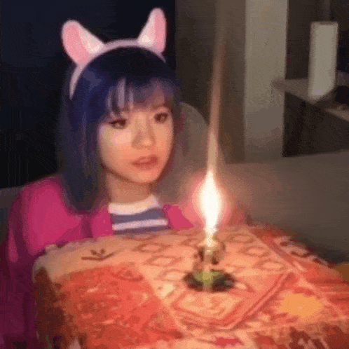 a girl with blue hair is blowing out a candle on a birthday cake .