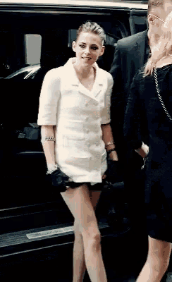a woman in a white jacket and shorts is standing in front of a car with the word mercedes on the door