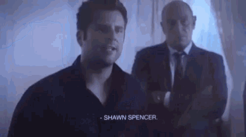 a man in a black shirt and tie is talking to another man in a suit and tie .