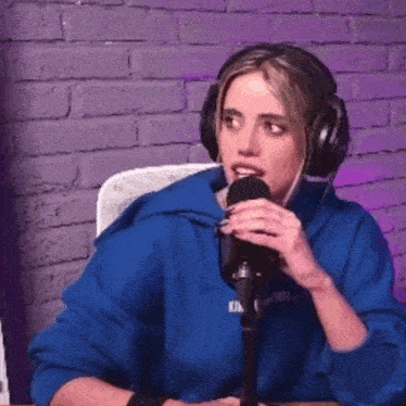 a woman in a blue hoodie is talking into a microphone while wearing headphones .