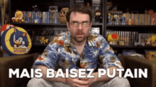 a man in a hawaiian shirt is sitting in front of a bookshelf with the words mais baisez putain written on it .