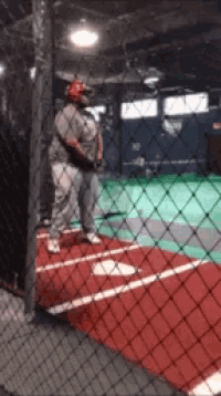 a man is standing on a baseball field behind a chain link fence holding a bat