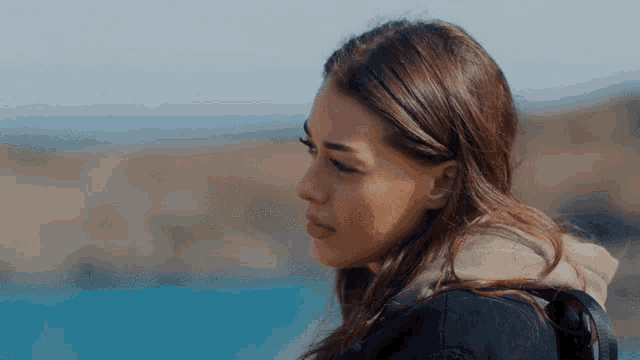 a woman in a black jacket looks at the ocean