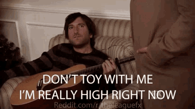 a man is sitting on a couch playing a guitar and talking to a woman .