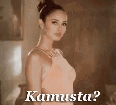 a woman in a dress is standing in a room with the words kamusta written on the screen .