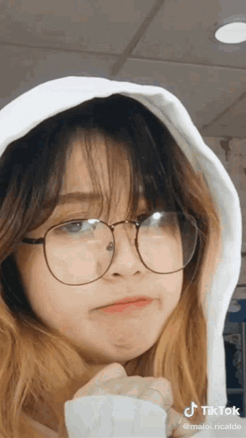 a girl wearing glasses and a white hoodie has a tiktok watermark on her face