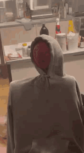 a person in a hoodie is sitting in a chair in a kitchen with a red ball on their head .