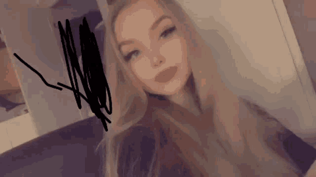 a woman with long blonde hair is taking a selfie in front of a mirror in a room .