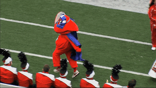 a mascot in a red and blue outfit is dancing on a field