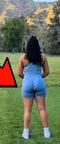 a woman in blue shorts is standing in a grassy field with a red triangle in the background .