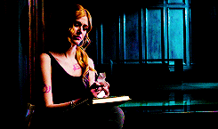 a woman in a black tank top is sitting in a dark room holding a book