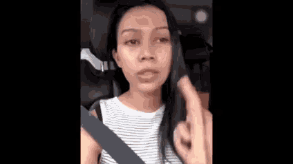 a woman is sitting in a car wearing a seat belt and giving a middle finger .